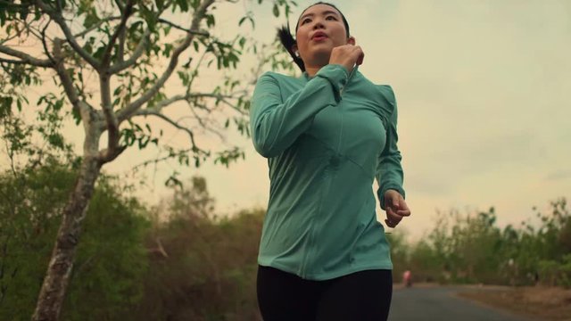 slow motion tracking gimbal shot on young and healthy Asian Korean woman running outdoors  in wood on sunset doing jogging workout in beautiful countryside road 