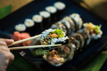 Eating roll sushi in japanese restaurant, hand with chopsticks closeup.. California Sushi roll set with salmon, vegetables.