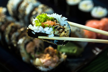 Eating roll sushi in japanese restaurant, hand with chopsticks closeup.. California Sushi roll set with salmon, vegetables.