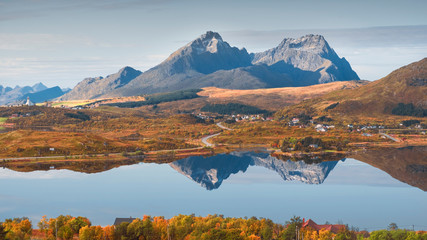 Autumn nature landscape of Norway on Lofoten islands. At the foot of the mountains, the town Borg is reflected in the mirror of the lake.