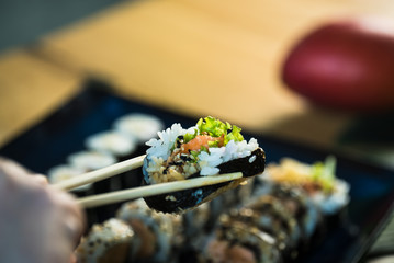 Eating roll sushi in japanese restaurant, hand with chopsticks closeup.. California Sushi roll set with salmon, vegetables.