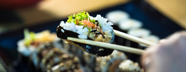 Eating roll sushi in japanese restaurant, hand with chopsticks closeup.. California Sushi roll set with salmon, vegetables.