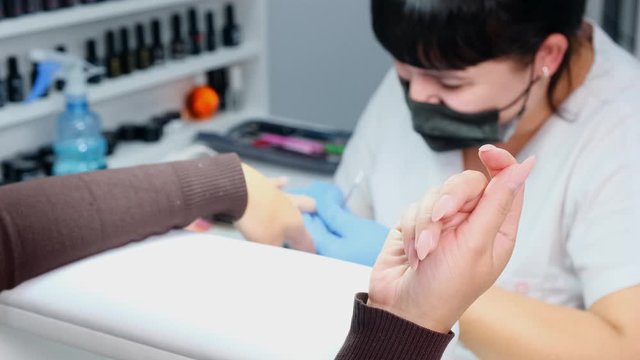 Manicurist files a nail with a nail file to a client. Manicure process, nail extension.
