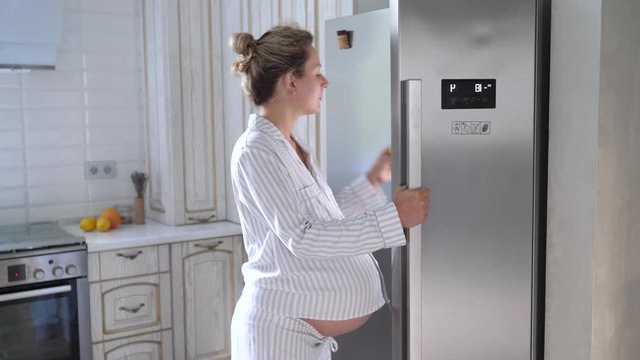 Young Pregnant Woman Looking Into Refrigerator For Something To Eat.