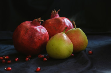 pomegranates and pears on a dark background and with scattered pomegranate seeds