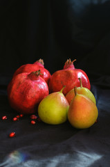 Fototapeta na wymiar pomegranates and pears on a dark background and with scattered pomegranate seeds