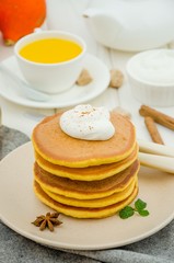 Obraz na płótnie Canvas Stack of spicy pumpkin pancakes on a plate with honey and whipped cream on a white wooden background. Rustic style. Fragrant autumn breakfast. Breakfast for Halloween.