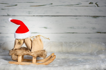 Weihnachtsmütze mit Schlitten und Geschenke im Schnee vor einem Holz Hintergrund