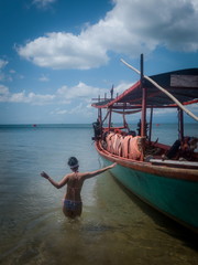 Asian Female Wearing a Bikini Holods Side of Fsihing Boat in Shallow Surf