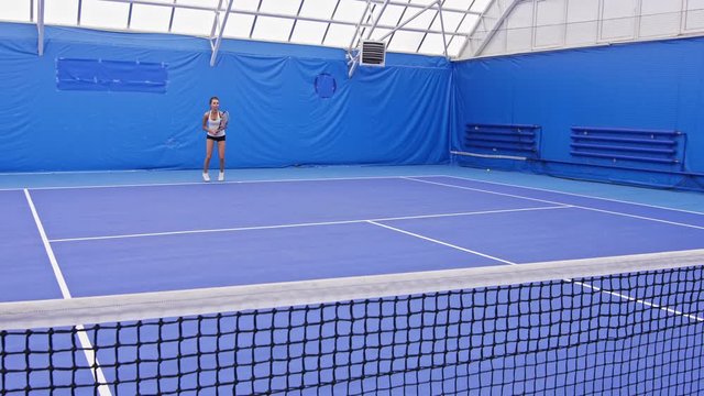 Tennis player training backhand and forehand on indoor blue court