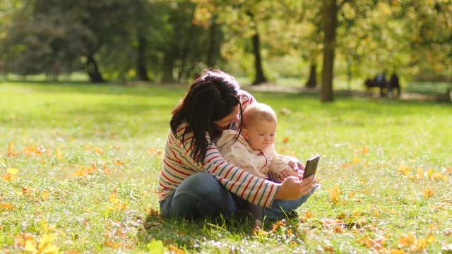 Young mother hugging toddler baby child daughter taking phone selfie picture enjoy spend time in park on a grass