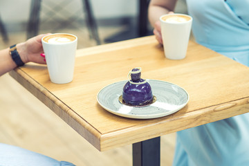 Tasty piece of cake on the table on background of two women's hands with coffee. Slice of cake on the plate on the wooden table at cafe.