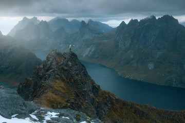 Winner woman in arms raised stands on top of a mountain under the gloomy sky of Norway  in Lofoten islands