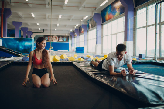 Young Woman Acrobat Learns To Jump On A Trampoline With Man Trainer