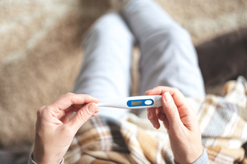 Disease. Home treatment. Flu and the common cold. A woman is sick at home, runny nose and flu. Body temperature measurement. In hands of a woman is an electronic thermometer.