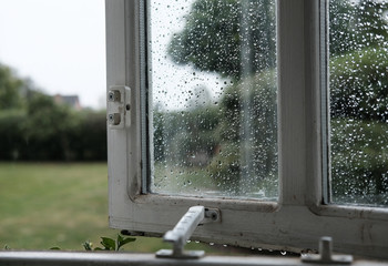 Opened home office window seen after a heavy downpour in a large back garden.