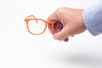 Gafas y lentes de colores y montura de plástico, de diseño, sobre fondo blanco y en la mano de una persona adulta; gafas con cristales graduados para mejorar la visión de las personas