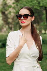 portrait of young woman in sunglasses. The girl in the white dress. Walk in the Park. Long-haired brunette. Female portrait. Young woman wearing sunglasses.