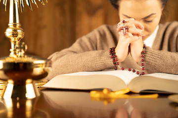 Christian woman with Bible praying in church by the altar. Woman kneeling in prayer with hands...