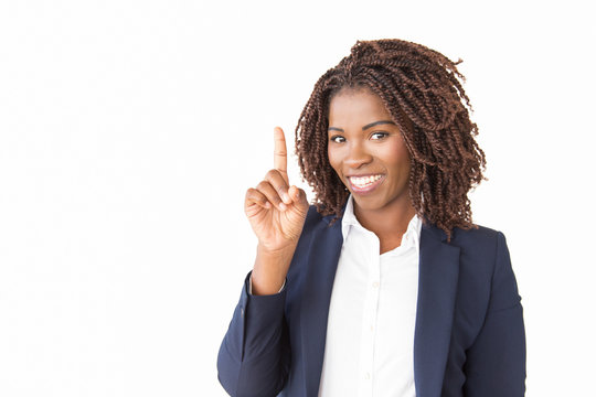 Happy young businesswoman pointing finger up at copy space. African American business woman standing isolated over white background, looking at camera, smiling. Advertising concept