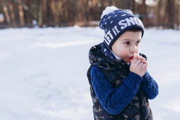 Little cute pretty boy in knitted hat sitting near window and looking on winter snowy park. Happines, joy, childhood, winter, christmas concept