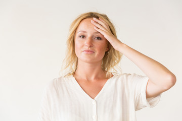 Fototapeta premium Upset woman with hand on forehead. Portrait of unhappy young woman standing with hand on forehead and looking at camera on grey background. Facial expression concept