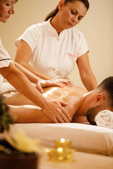 Two female therapists massaging man's back at the spa.