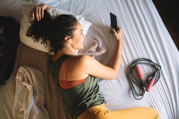 Young woman after training lying on bed and listening music