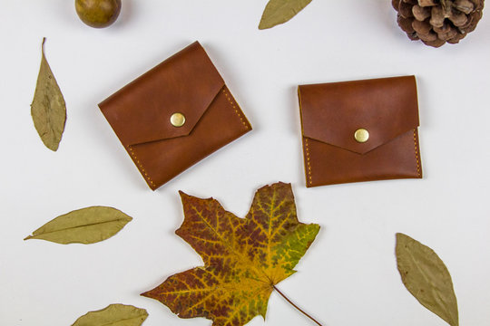 leather wallets and dry autumn leaves on a white background, top view
