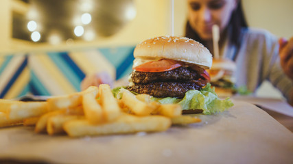 A big juicy burger with two cutlets, vegetables, sauce and french fries on the table in a cafe.