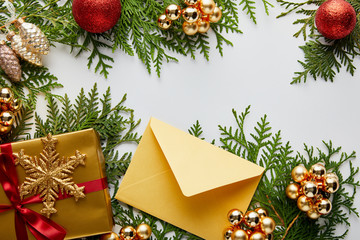 top view of shiny golden Christmas decoration, gift and envelope on green thuja branches isolated on white