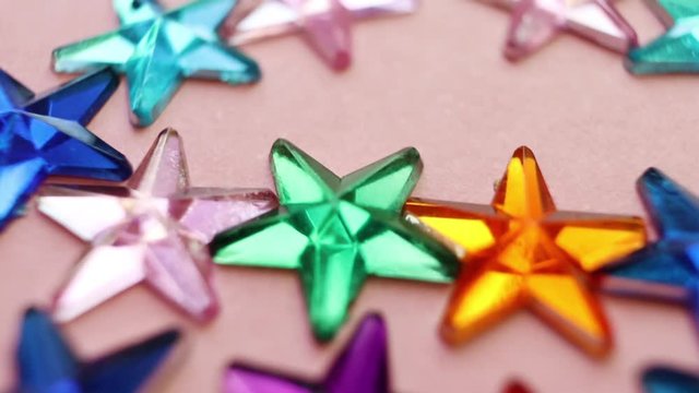 Rhinestones in the form of multi-colored stars on a pink background. Macro. The concept of a holiday, party, fun.