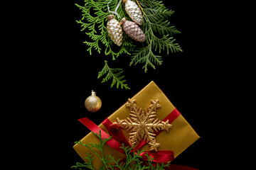 top view of shiny golden Christmas decoration, green thuja branches and gift box isolated on black