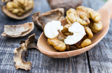Walnuts and walnut kernels lie in a spoon on a rustic old wooden table. Kernels of walnuts.