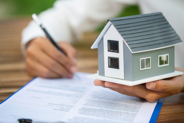 Gray roof house Put on the hands of the sales representative. The hands of a businessman signing a house purchase contract.Sign the contract, sign on the official document. House trading ideas