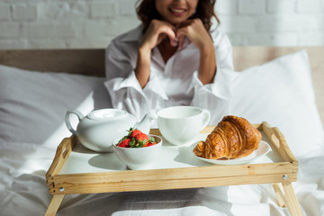 Obraz na płótnie Canvas cropped view of woman in white shirt having breakfast in bed at morning