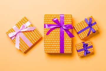 wrapped Christmas or other holiday handmade present in paper with purple and pink ribbon on orange background. Present box, decoration of gift on colored table, top view
