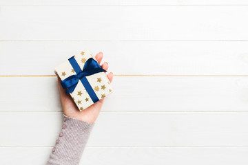 Woman arms holding gift box with colored ribbon on white wooden table background, top view copy...