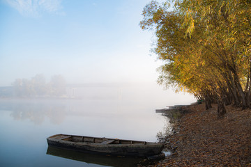 Autumn calm morning on meadow with a boat on the river. Beautiful sunrise over field with sunlight and mist.