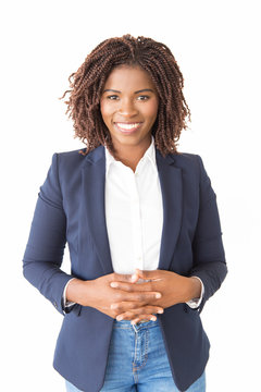 Happy joyful female agent posing with clasped hands. Young African American business woman standing isolated over white background, looking at camera. Successful professional concept