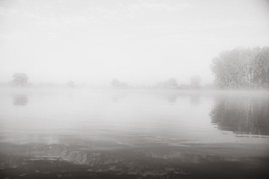 Autumn calm morning on meadow with river. Beautiful sunrise over field with sunlight and mist.Black and white photo
