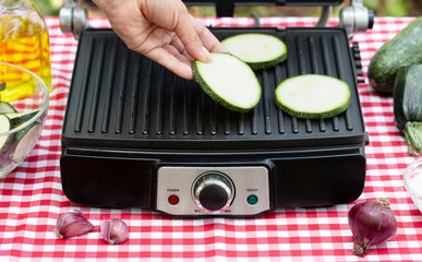 Female hand puts sliced zucchini on grill