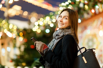 Picture of woman with phone in hand on street in evening on blurred background with garland