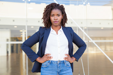 Serious successful female manager posing near office building. Young African American business...