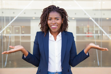 Cheerful confused female manager posing outside. Young black business woman standing near outdoor...