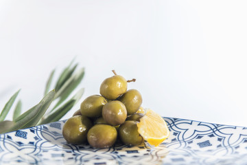Obraz na płótnie Canvas Homemade green olives in a chinese plate with olive tree branches and a piece of lemon on a white background, isolated, close up