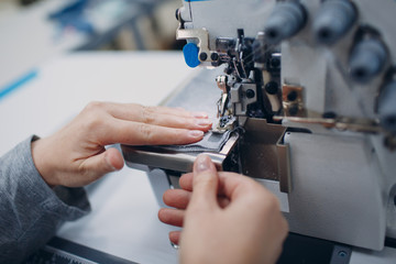 Young beautiful seamstress sews on sewing machine in factory