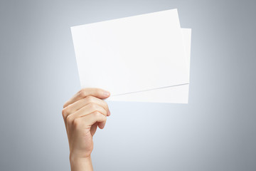 Hand holding two small sheets of paper (tickets, flyers, invitations, coupons, banknotes, etc.) on gray background