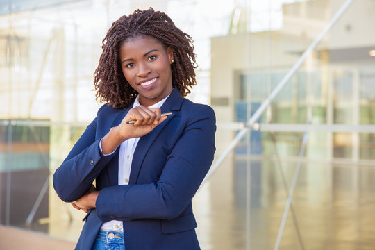 Happy cheerful manager pointing at copy space with pen. Young African American business woman holding pen, looking at camera, smiling. Advertising concept