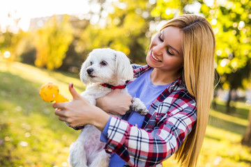 Beautiful woman is playing with her Maltese dog in the park.	